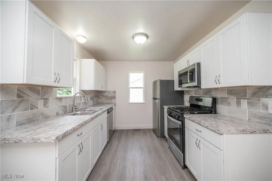 Kitchen with decorative backsplash, stainless steel appliances, light countertops, white cabinets, and light wood-style floors