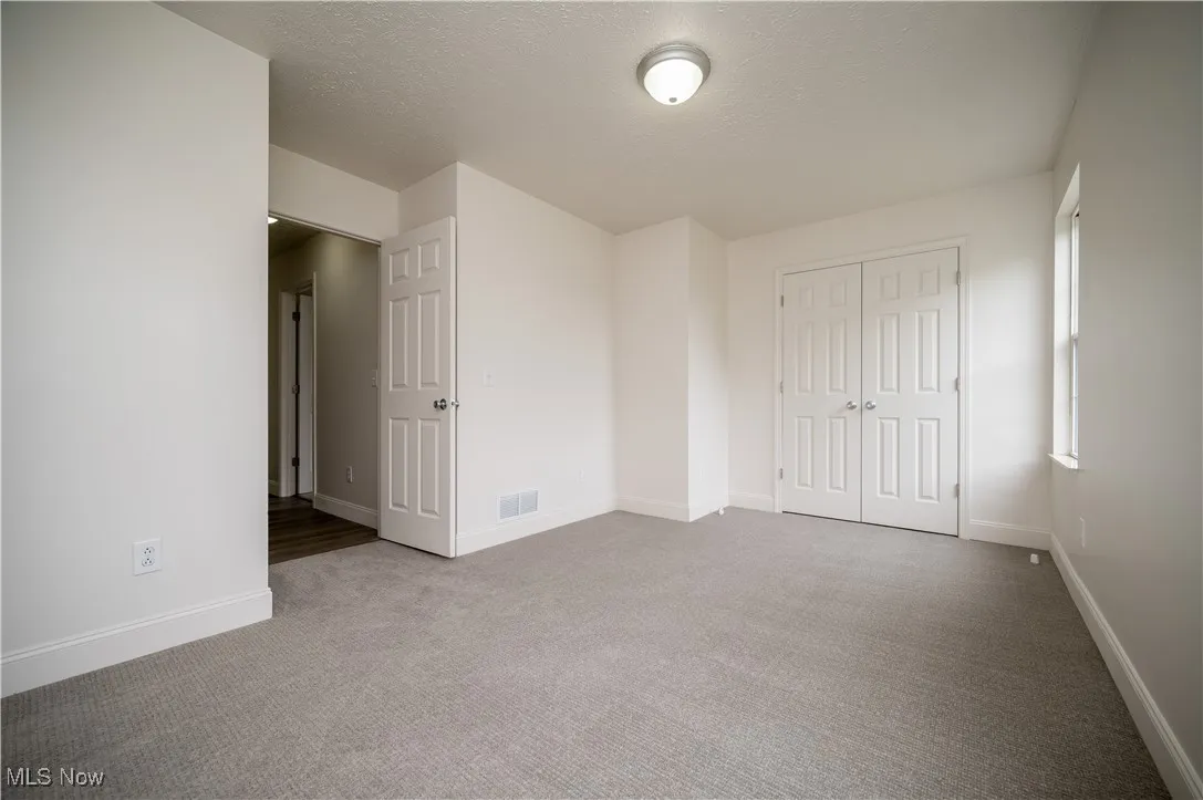 Unfurnished bedroom featuring light colored carpet, a textured ceiling, and a closet