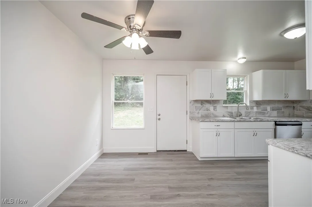 Kitchen featuring white cabinets, light wood-type flooring, tasteful backsplash, stainless steel dishwasher, and a ceiling fan