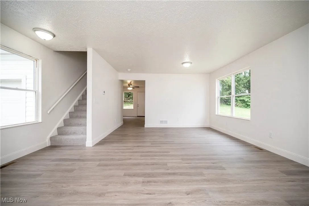 Unfurnished living room with light wood-style flooring, a textured ceiling, stairs, and ceiling fan