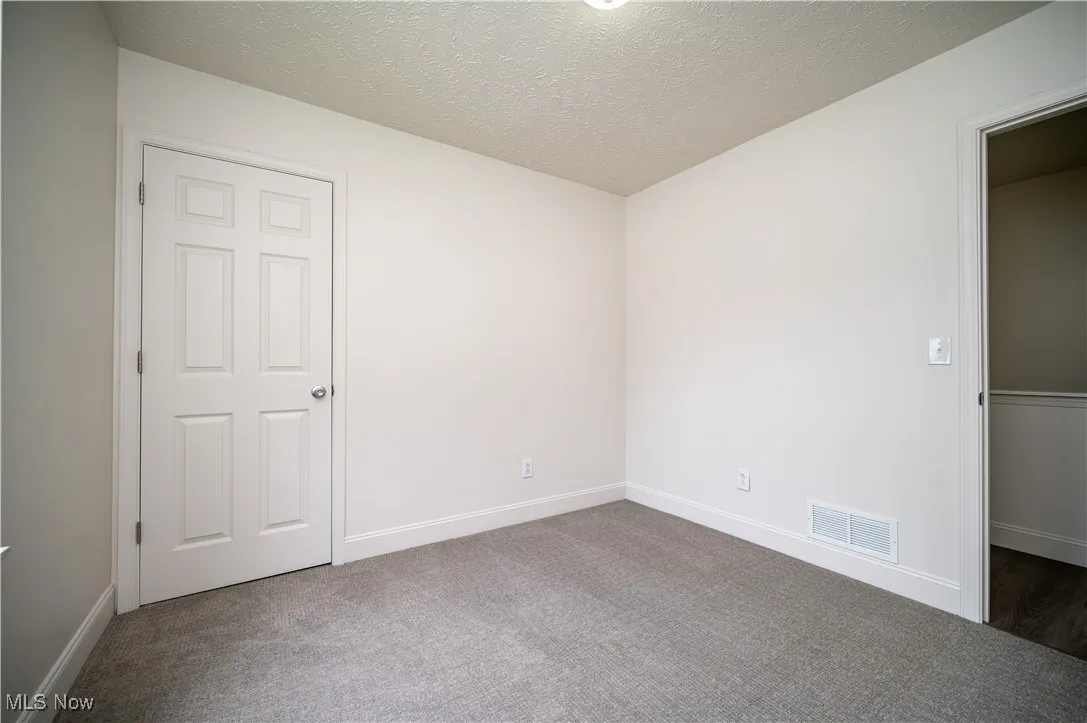 Carpeted empty room featuring a textured ceiling and baseboards