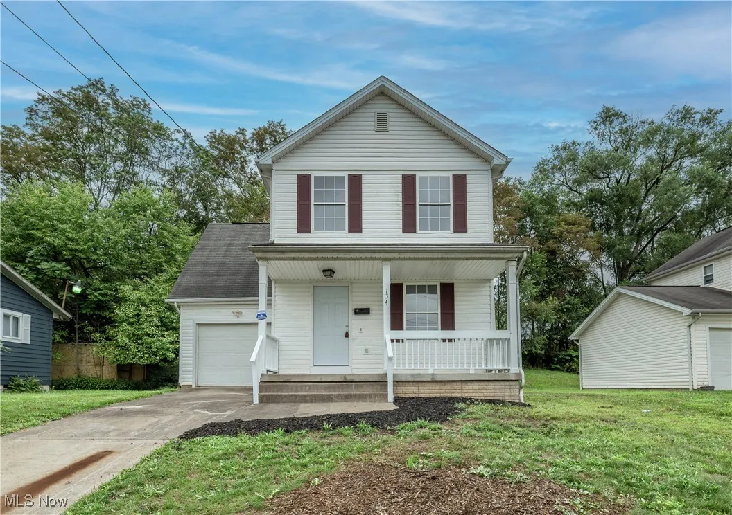 Traditional-style house featuring a porch, concrete driveway, a shingled roof, a front lawn, and a garage