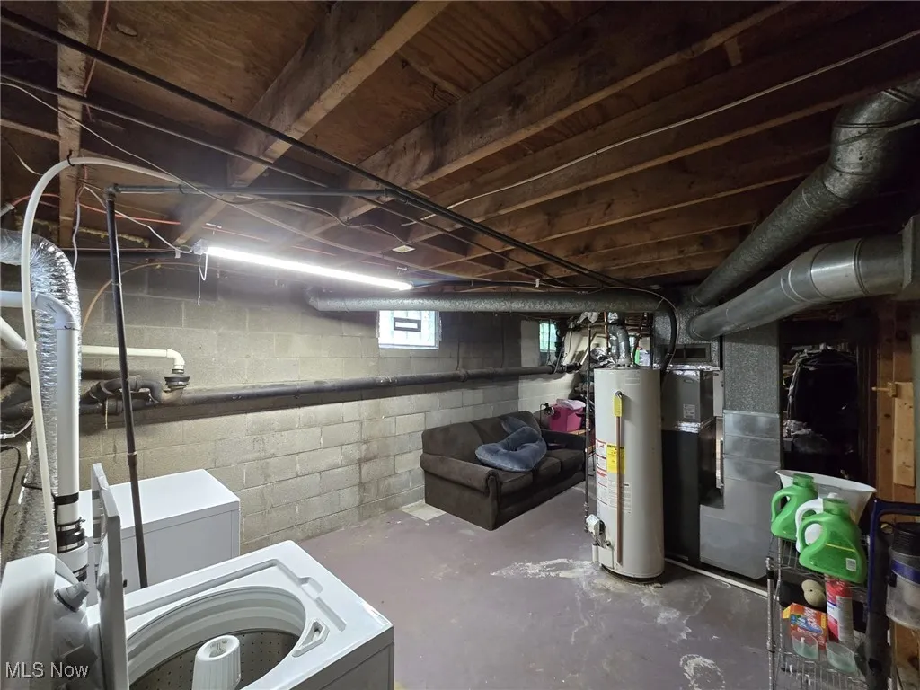 Below grade area with gas water heater, heating unit, and white refrigerator