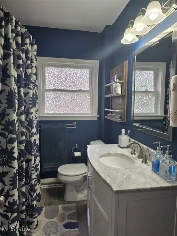 Full bath with dark wood-type flooring, vanity, and curtained shower