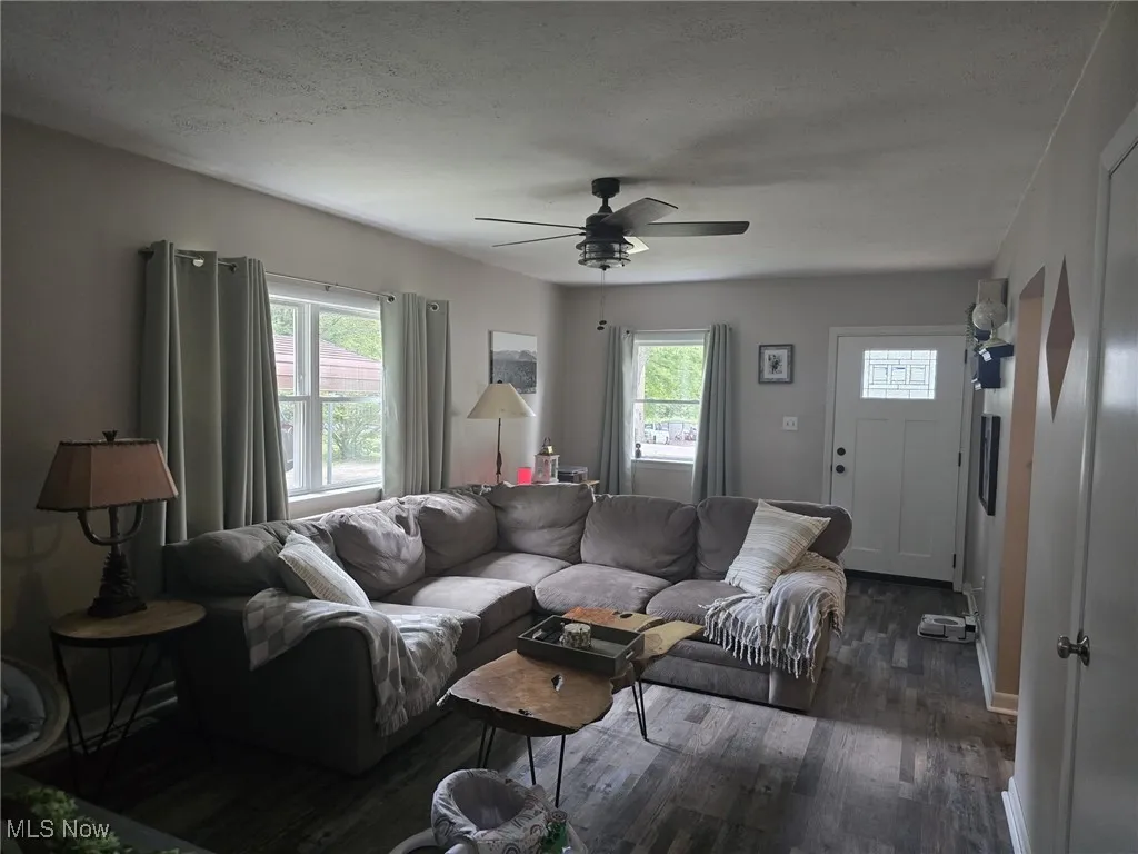 Large living room featuring natural light, dark wood-style  flooring, ceiling fan, and a textured ceiling