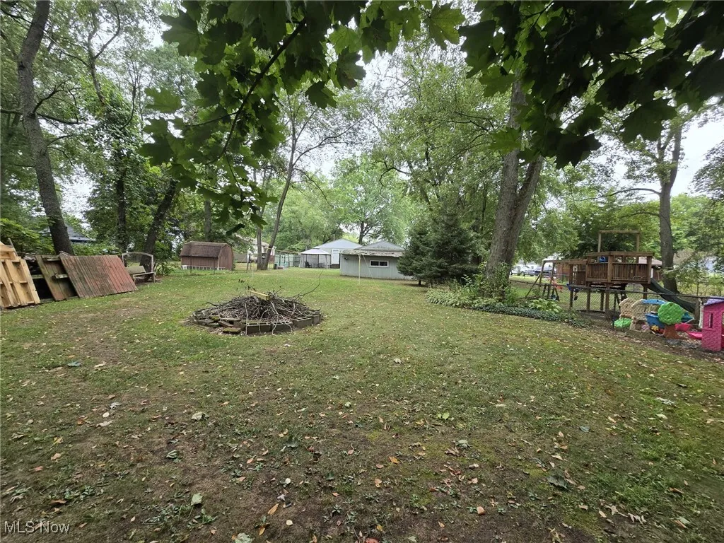 View of yard with a playground, an outdoor fire pit, a deck, and view of scattered trees
