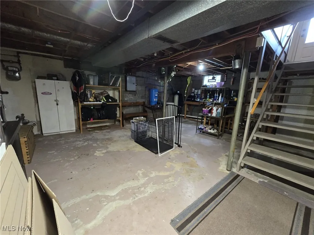 Unfinished below grade area featuring stairs, electric panel, and a water pressure tank