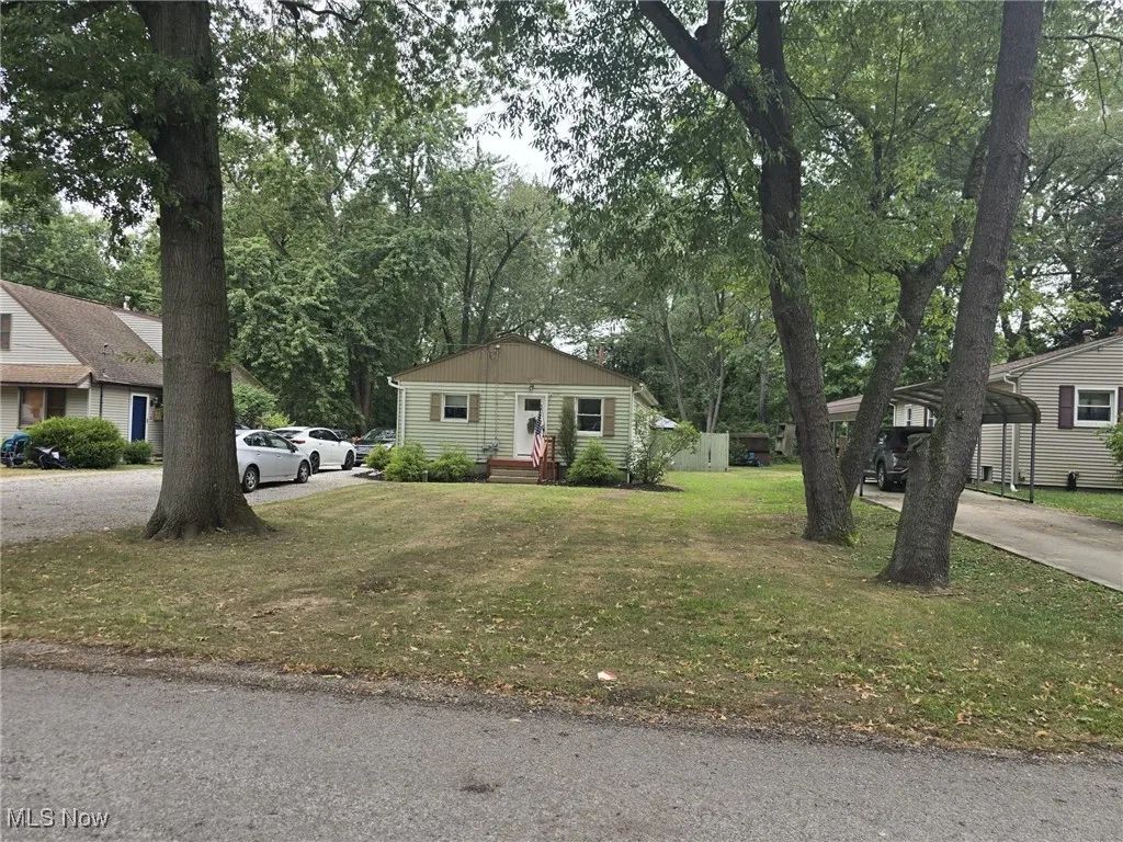 View of front facade with driveway, a front lawn, and view of wooded area