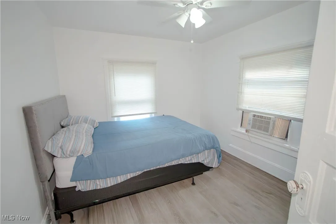 Bedroom with light wood-style floors, a ceiling fan, multiple windows, and cooling unit