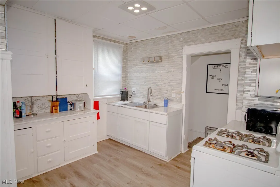 Kitchen with decorative backsplash, white cabinetry, light wood-type flooring, light countertops, and a paneled ceiling