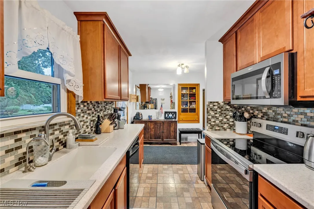 Kitchen featuring stainless steel appliances, backsplash, light stone countertops, and brown cabinets