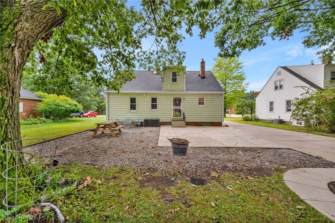 Rear view of house with a shingled roof, a patio area, a chimney, a yard, and entry steps
