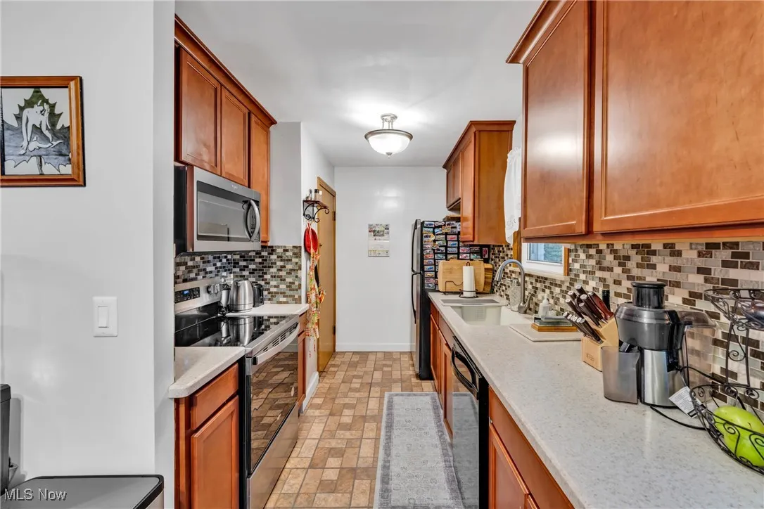 Kitchen with stainless steel appliances, decorative backsplash, brown cabinetry, and light stone counters