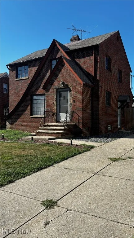 View of front of property with brick siding, a chimney, and a front yard