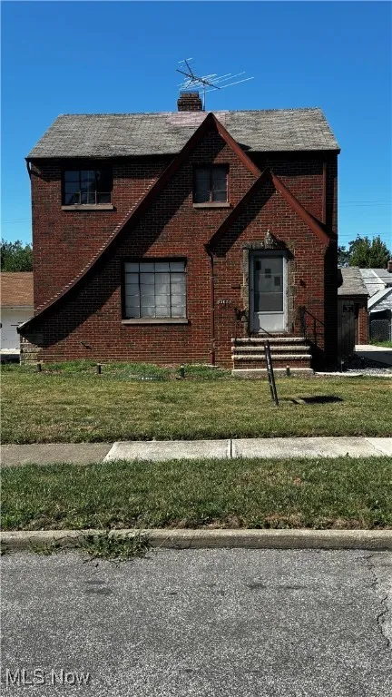 View of front of home featuring a chimney, brick siding, and a front yard