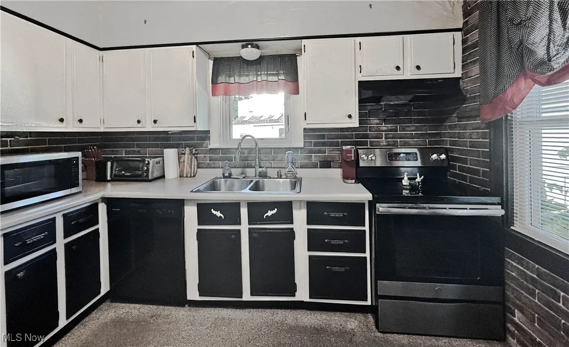 Kitchen with appliances with stainless steel finishes, light countertops, white cabinets, tasteful backsplash, and under cabinet range hood