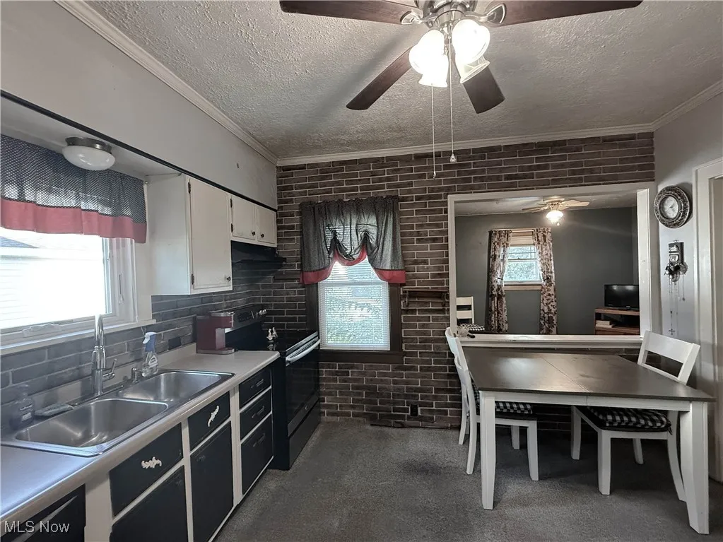 Kitchen featuring brick wall, light countertops, black electric range, white cabinetry, and a textured ceiling