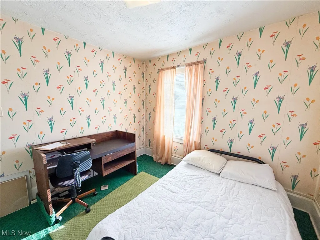 Bedroom with wallpapered walls, a textured ceiling, and carpet
