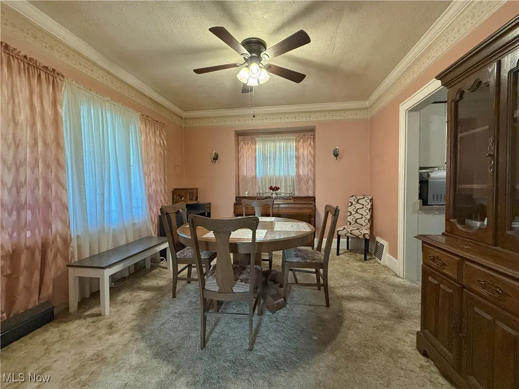 Dining area with light carpet, a textured ceiling, ceiling fan, and ornamental molding