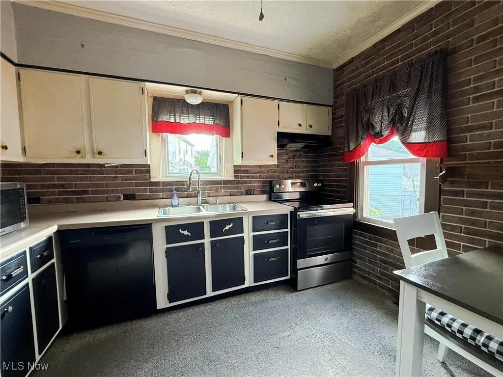 Kitchen featuring light countertops, stainless steel appliances, healthy amount of natural light, brick wall, and crown molding