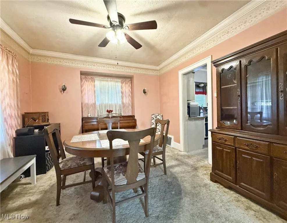 Dining area with a textured ceiling, light colored carpet, ceiling fan, and ornamental molding