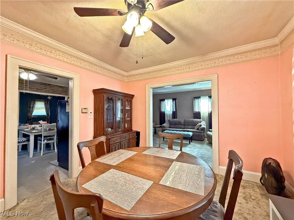 Carpeted dining space with a textured ceiling, a ceiling fan, and crown molding