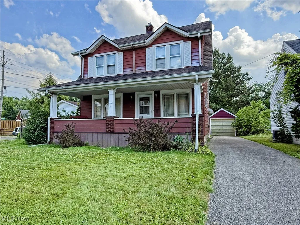 View of front of house featuring an outbuilding, a porch, a detached garage, a front lawn, and a chimney