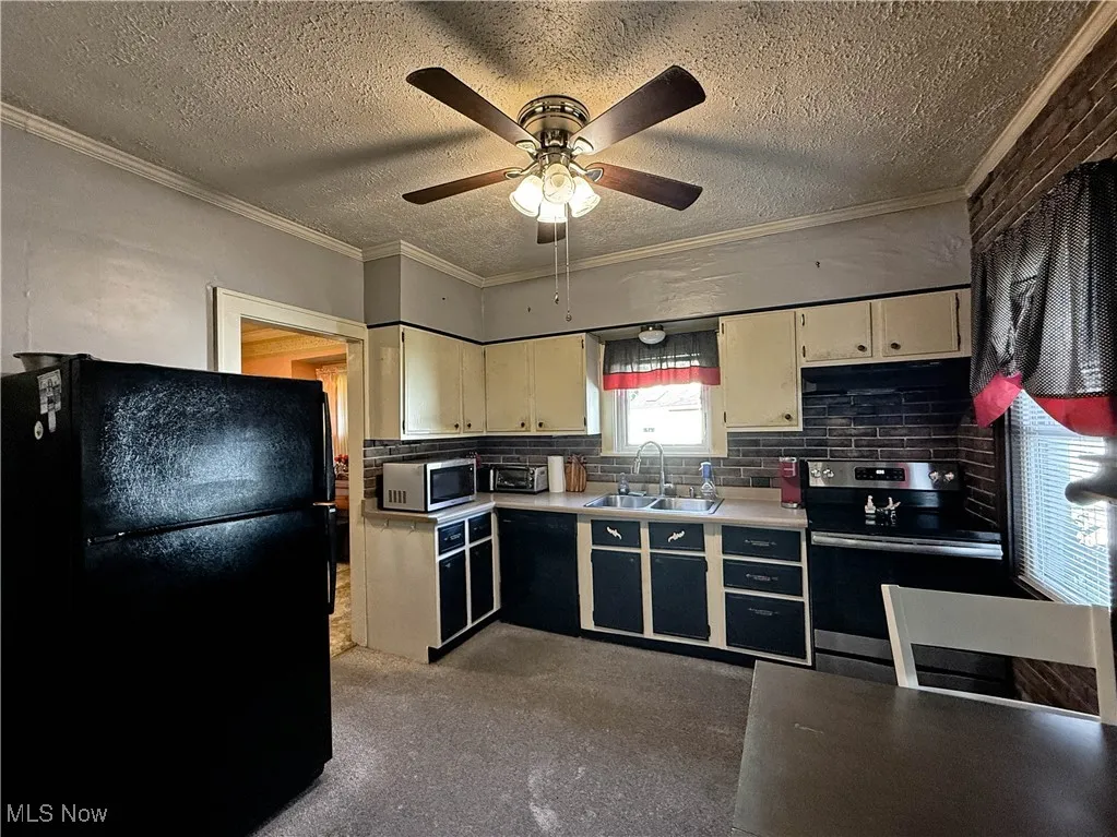 Kitchen featuring light countertops, black appliances, backsplash, crown molding, and a textured ceiling