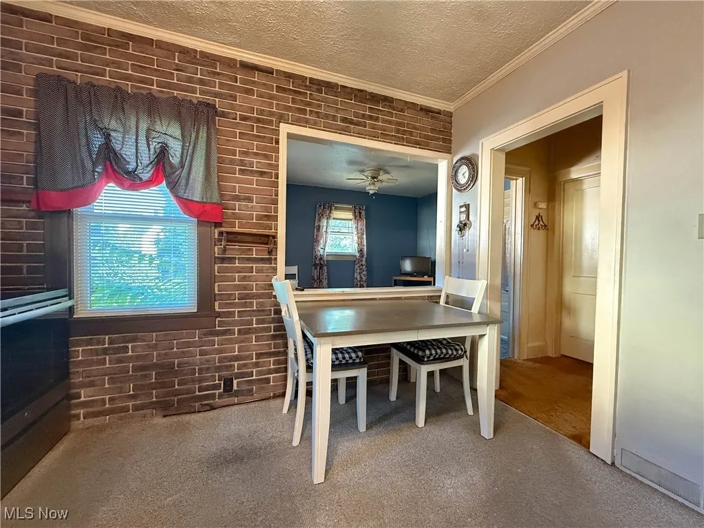 Carpeted dining room with brick wall, a textured ceiling, crown molding, and ceiling fan