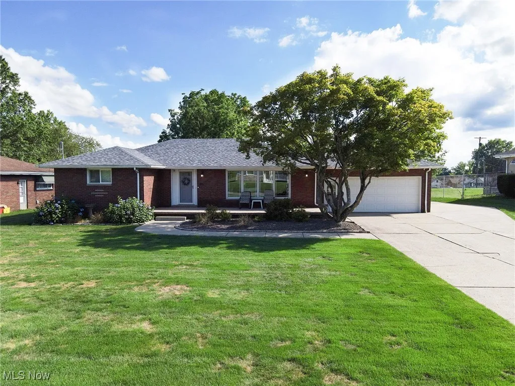 Single story home featuring a front lawn, concrete driveway, brick siding, a porch, and an attached garage