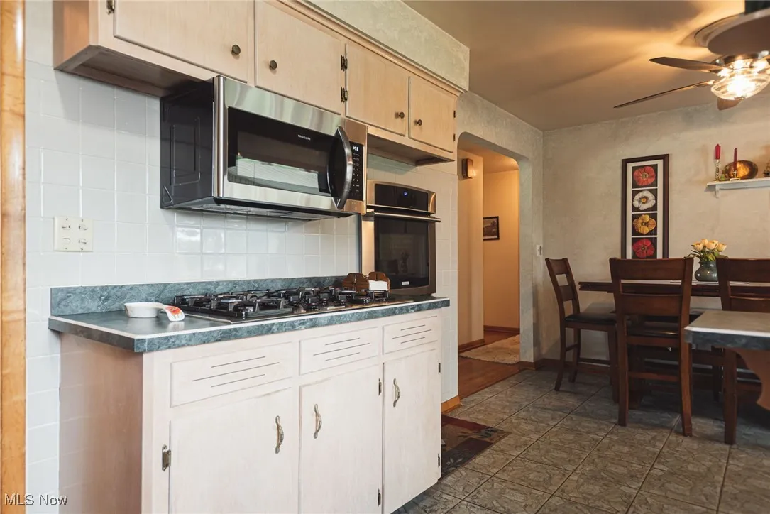 Kitchen featuring backsplash, arched walkways, light brown cabinets, appliances with stainless steel finishes, and dark countertops
