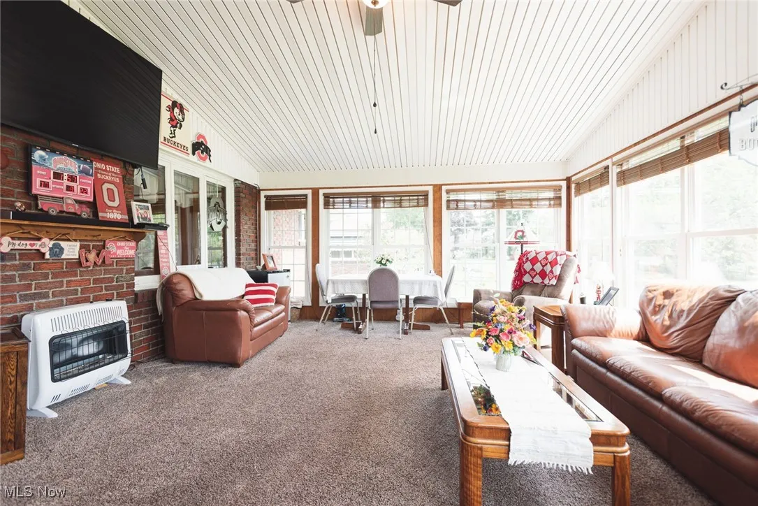 Living area with lofted ceiling, heating unit, carpet floors, a ceiling fan, and a fireplace