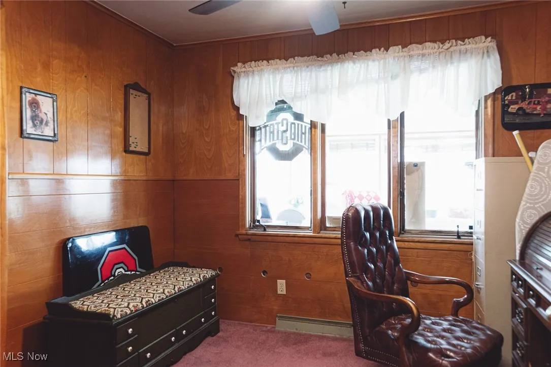 Carpeted office space with wood walls, a baseboard radiator, and a ceiling fan