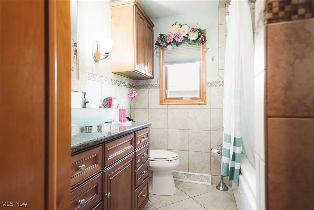 Full bathroom with tile walls, vanity, light tile patterned floors, and shower / tub combo