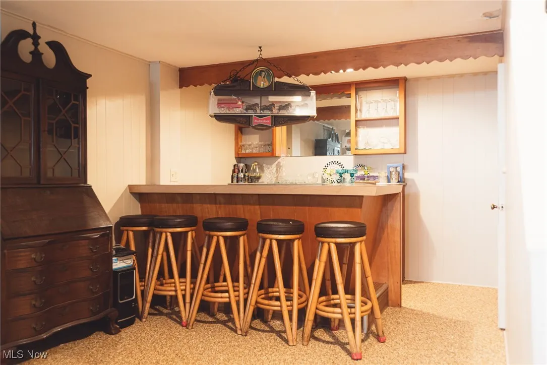 Indoor dry bar with light countertops, wooden walls, and brown cabinetry
