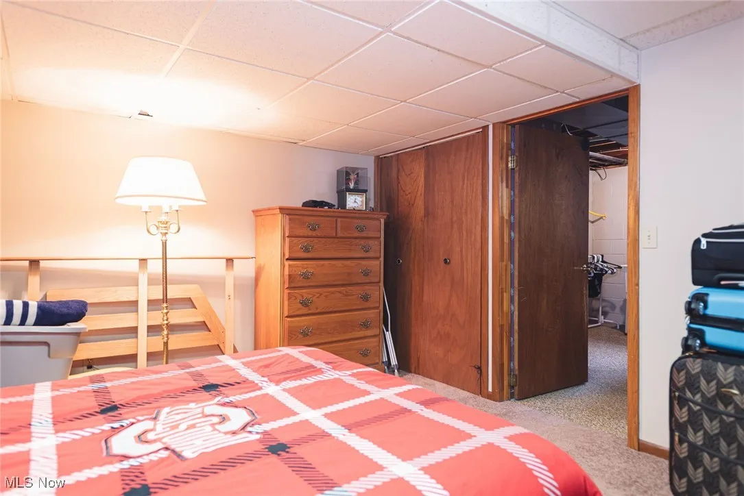 Bedroom with a closet, a drop ceiling, and light carpet