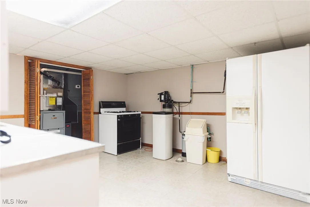 Kitchen with white appliances, a paneled ceiling, light floors, and white cabinets