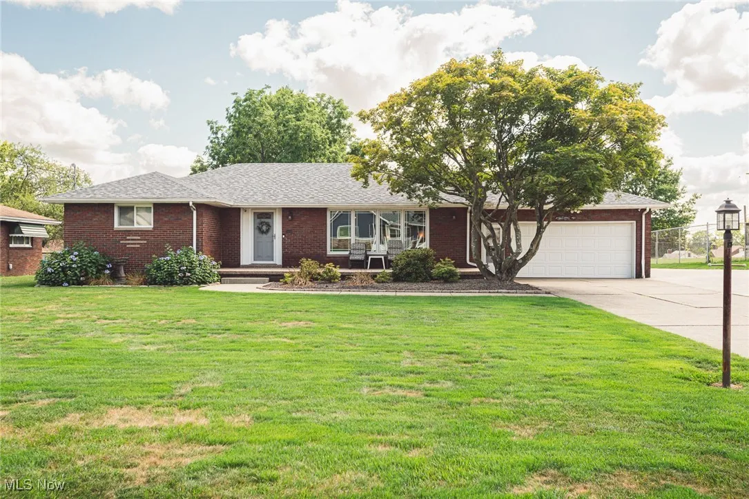 Ranch-style house with driveway, a front yard, brick siding, a garage, and roof with shingles