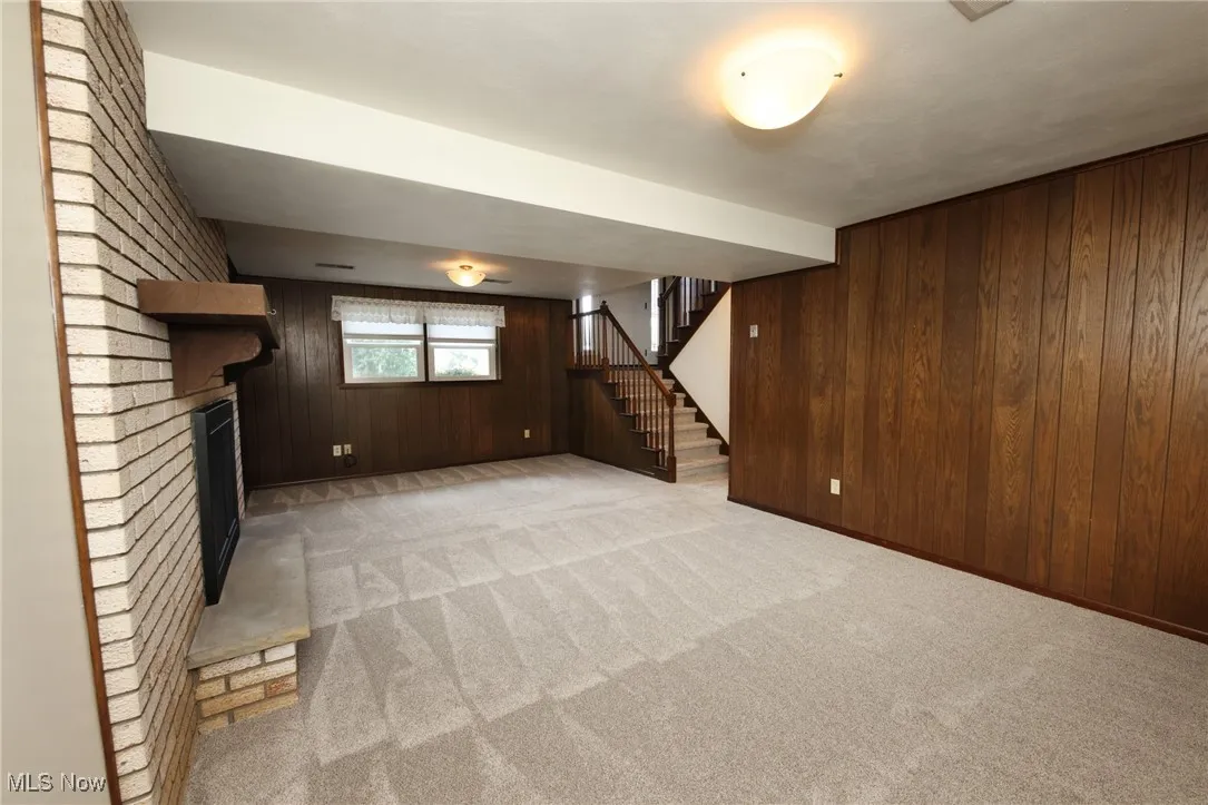 Basement featuring wooden walls, light colored carpet, stairway, and a brick fireplace