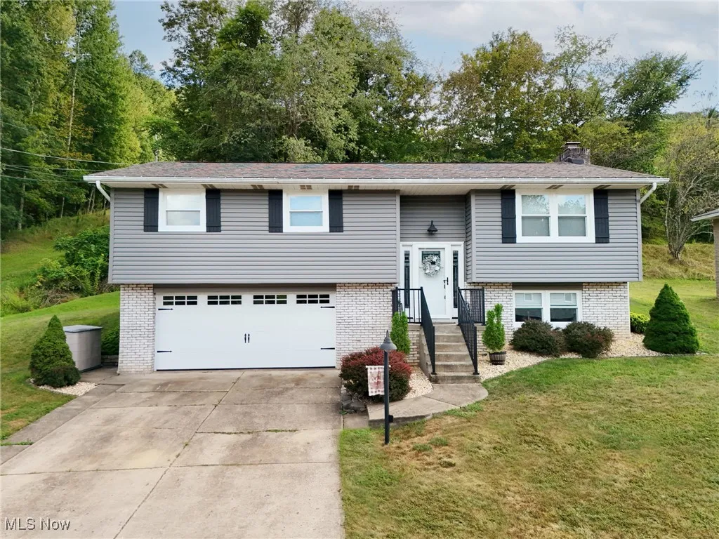Raised ranch with brick siding, a front yard, a chimney, and concrete driveway