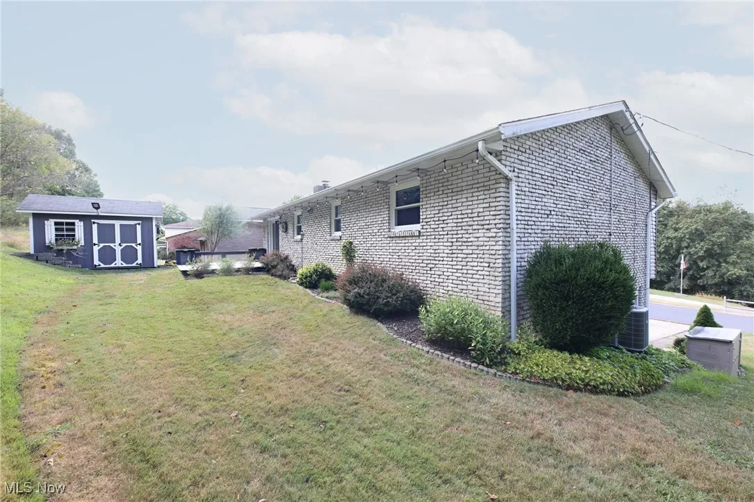 View of side of home featuring a storage unit, a lawn, and brick siding