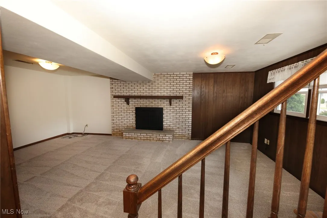 Stairway with wooden walls, carpet, and a brick fireplace