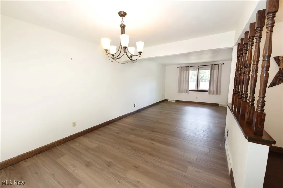 Unfurnished room with dark wood-style floors and a chandelier