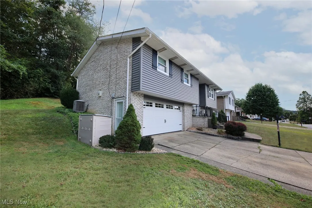View of property exterior featuring brick siding, concrete driveway, a garage, and a lawn