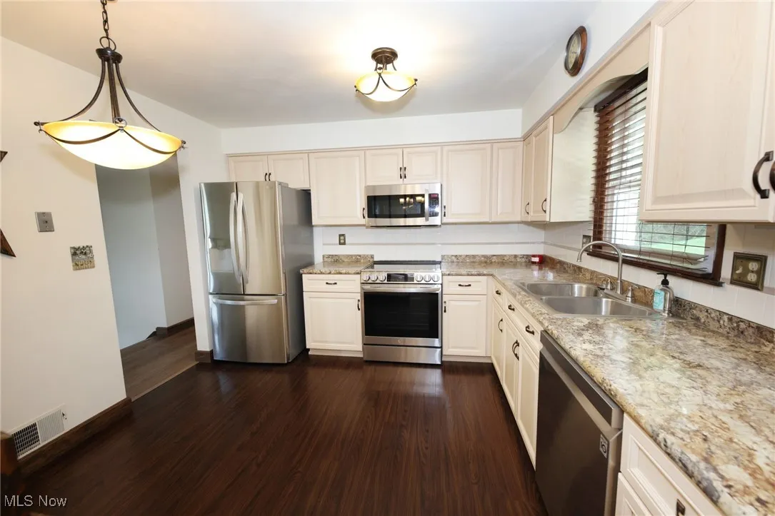 Kitchen featuring stainless steel appliances, dark wood-type flooring, pendant lighting, and light stone counters