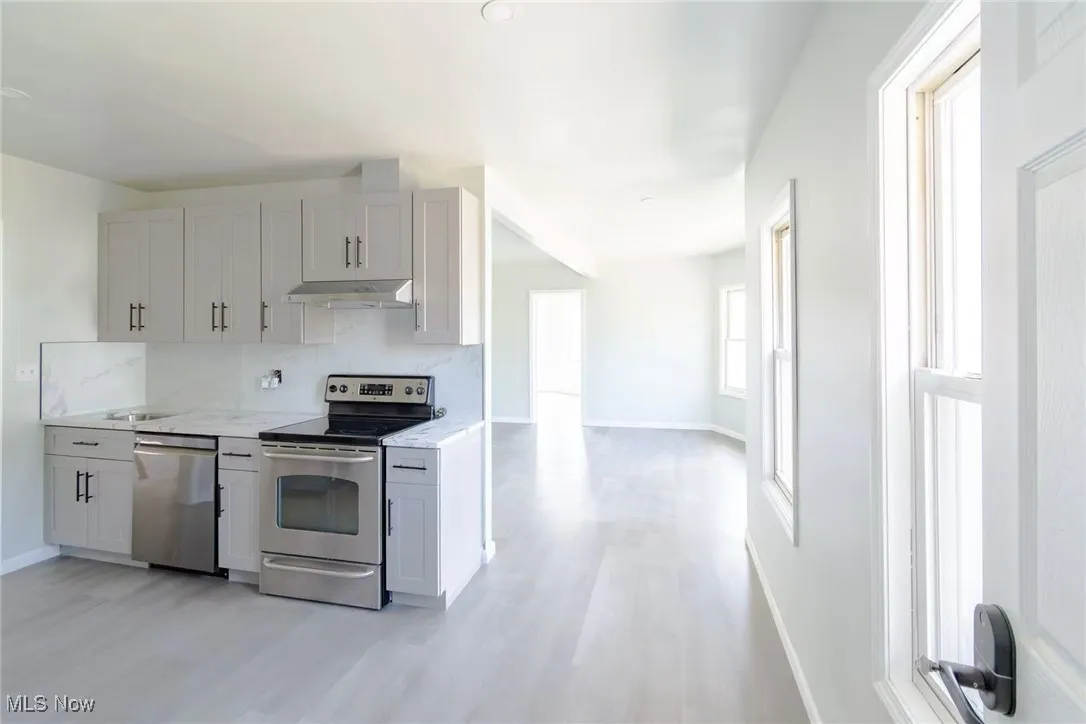 Kitchen featuring stainless steel appliances, backsplash, light wood-style floors, under cabinet range hood, and light stone countertops