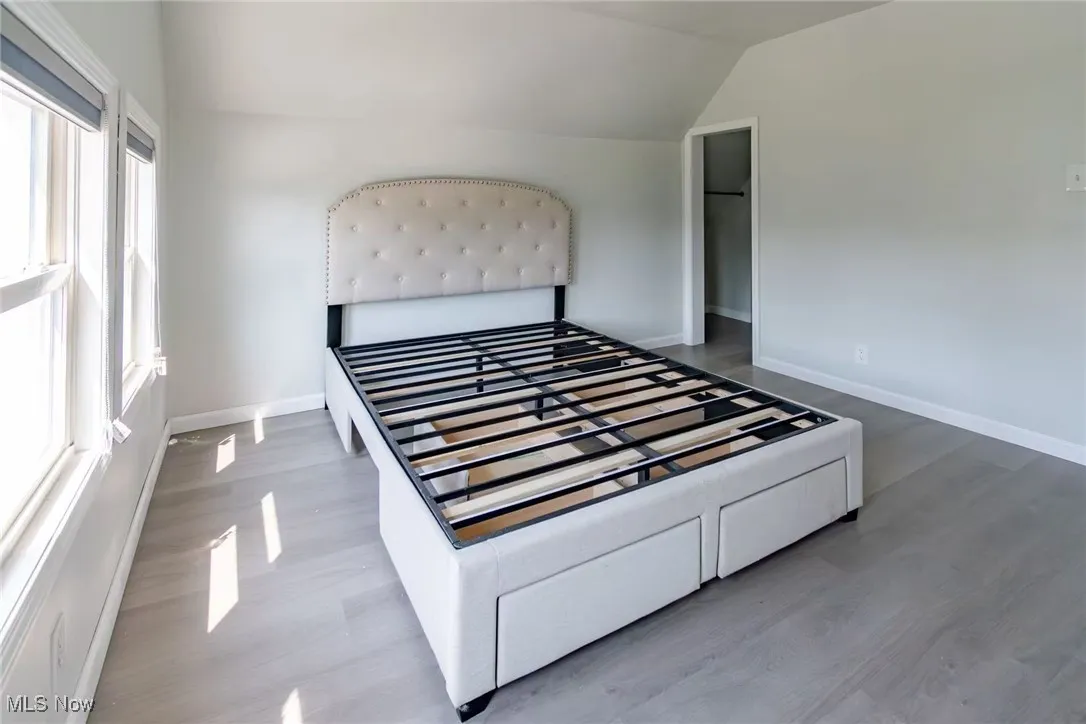 Unfurnished bedroom featuring vaulted ceiling, wood finished floors, and a walk in closet