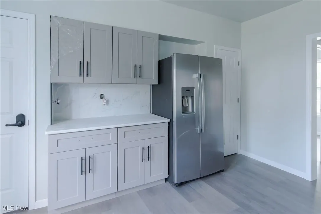 Kitchen featuring stainless steel fridge, light wood finished floors, tasteful backsplash, and gray cabinetry