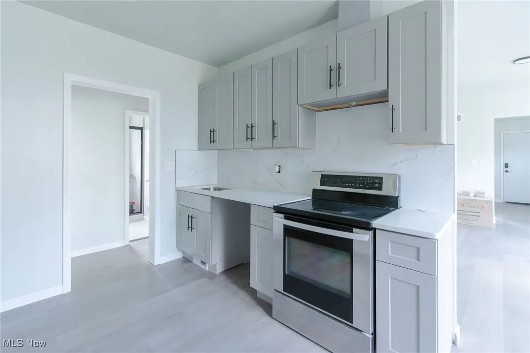 Kitchen featuring stainless steel range with electric stovetop, tasteful backsplash, gray cabinets, and light wood-style flooring