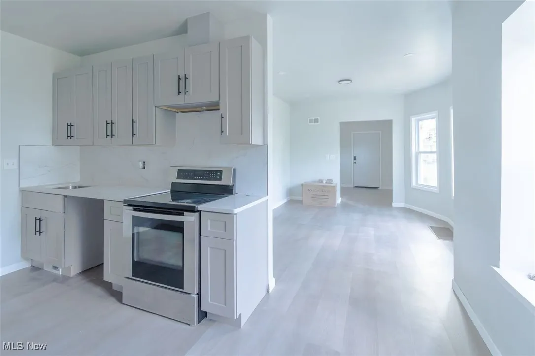 Kitchen featuring stainless steel electric range oven, decorative backsplash, light wood-type flooring, and light stone countertops